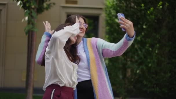 两个姐妹拥抱在一起 笑着挥动着胳膊 用手机和母亲在电视上交谈 站在城市公园的一块空地上 — 图库视频影像