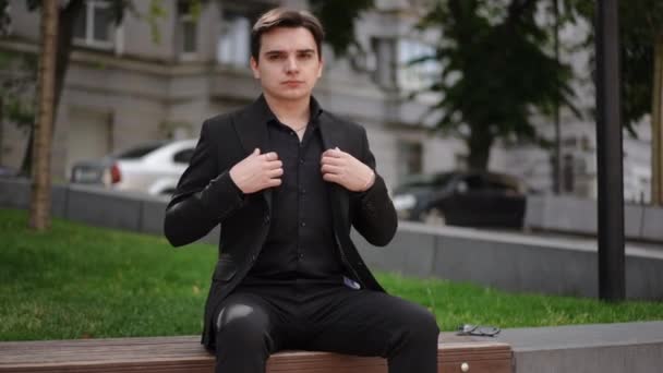 Ένας Νεαρός Κοστούμι Προσαρμόζει Σακάκι Του Και Χαμογελάει Ενώ Κάθεται — Αρχείο Βίντεο