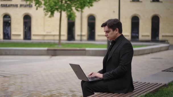 Biznesmen Garniturze Siedzi Ławce Parku Miejskim Szybko Pisze Klawiaturze Laptopa — Wideo stockowe