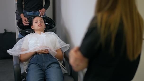 一位女理发师讲述了护发品的好处 而一位女客户则躺在椅子上 头上涂满了香油 — 图库视频影像