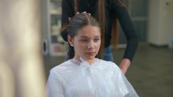 一个女孩坐在一把湿头发的椅子上 坐在沙龙里 理发师学习如何正确地梳理湿头发 透过镜子里的倒影射击 — 图库视频影像