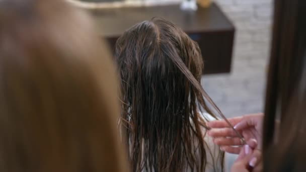 后视镜 从肩膀后面射出 一个女孩坐在一把湿头发的椅子上 坐在沙龙里 女理发师检查一缕湿透的女孩的头发是否有力气 后续行动 — 图库视频影像