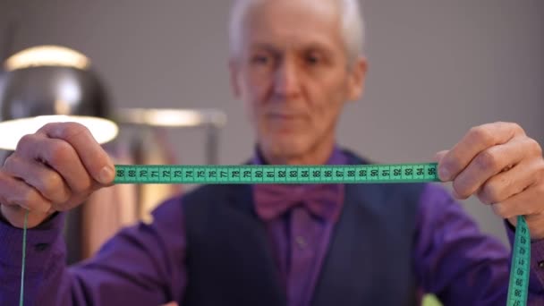 前景には テープを測定するテーラーがあり 高齢者の手にはスタイリッシュな男性がいます モダンハウスの部屋に立っている男 — ストック動画