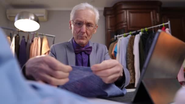 Äldre Modedesigner Med Glasögon Sitter Och Arbetar Vid Ett Bord — Stockvideo