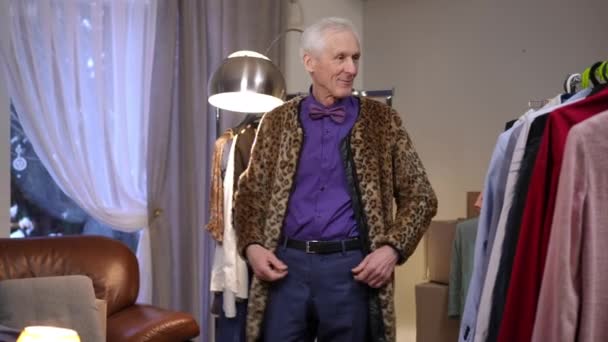 Улыбающийся Экстравагантный Пожилой Мужчина Модельер Рассматривает Одежду Висящую Передвижной Вешалке — стоковое видео