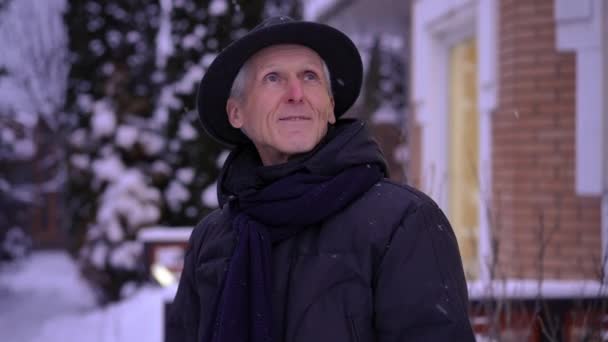 Starszy Mężczyzna Kapeluszu Obserwuje Padający Śnieg Stojący Zewnątrz Przy Ganku — Wideo stockowe