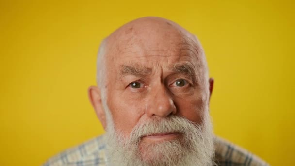 一个上了年纪的白胡子男人穿着衬衫的画像 由于视力不好 在黄色背景下被隔离 这个人看着摄像机 后续行动 — 图库视频影像