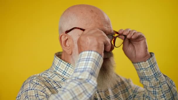 高齢の灰色のひげを被った男の肖像画は シャツを着て眼鏡をかけ 額の下から遠くまで見上げ 黄色の背景に隔離された おんな は半分 ぜんぶん かっている — ストック動画