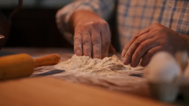 一个无法辨认的老人坐在厨房里 双手在面粉上挖了一个洞 这个洞躺在一张木制桌子上 从一个黏土罐子里往里面倒水 后续行动 — 图库视频影像