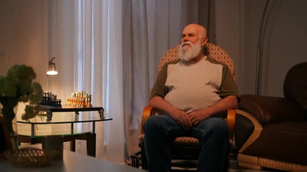 Tシャツとジーンズの孤独な年配のひげの男は 彼の家の居心地の良いリビングルームで ロッキングチェアに座って岩 — ストック動画