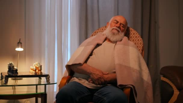 Tシャツとジーンズに包まれた孤独な年配のひげの男 彼の家の居心地の良いリビングルームでロッキングチェアで眠る — ストック動画
