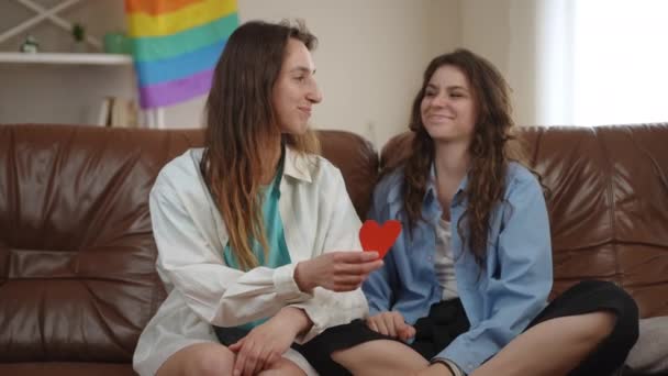 Две Девушки Сидят Диване Гостиной Фоне Радужного Флага Девушка Дает — стоковое видео