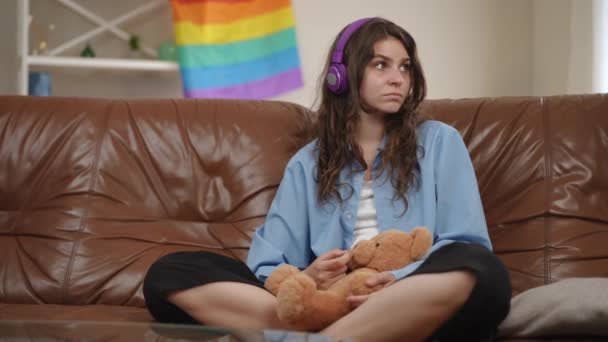 Uma Menina Senta Sofá Usando Fones Ouvido Sem Fio Segurando — Vídeo de Stock