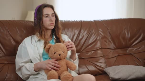 Dziewczyna Słucha Muzyki Siedząc Kanapie Słuchawkach Bezprzewodowych Dziewczyna Trzyma Pluszowego — Wideo stockowe