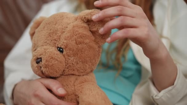 一个坐在客厅里皮沙发上的女孩手里拿着一只玩具熊的特写 — 图库视频影像