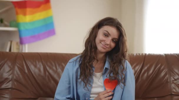 Girl Sits Sofa Room Backdrop Rainbow Flag Holds Red Cardboard — Stock Video