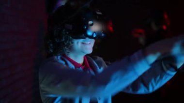 Yakın plan. VR kasklı ve elinde kumandayla bir genç ellerini mavi ışıklı bir VR kulübünün karanlık odasında hareketlendiriyor.