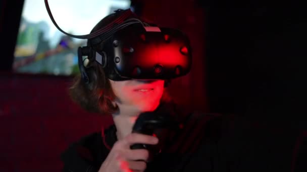 一个戴着Vr眼镜和手持控制器的青少年在玩电子游戏时模仿射箭 年轻人在一间黑暗的房间里 在Vr俱乐部有红灯 后续行动 — 图库视频影像