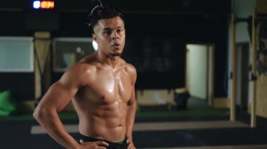 Ağır çekim. Yakın plan. Rastalı genç bir ırk adamı derin derin nefes alıyor ve spor salonunda dururken kameraya bakıyor.