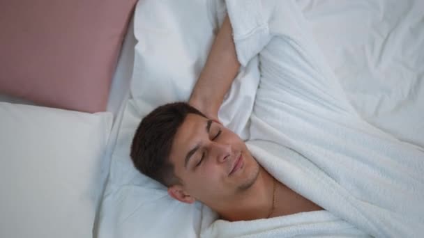 Zbliżenie Młody Mężczyzna Białym Szlafroku Leży Łóżku Swojej Sypialni Śni — Wideo stockowe