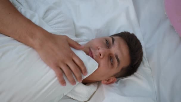 顶部视图 一个身穿白色浴衣的年轻人双手抱着枕头躺在卧室的床上 — 图库视频影像