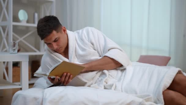 Молодий Чоловік Білому Халаті Ентузіазмом Читає Книгу Лежачи Ліжку Спальні — стокове відео
