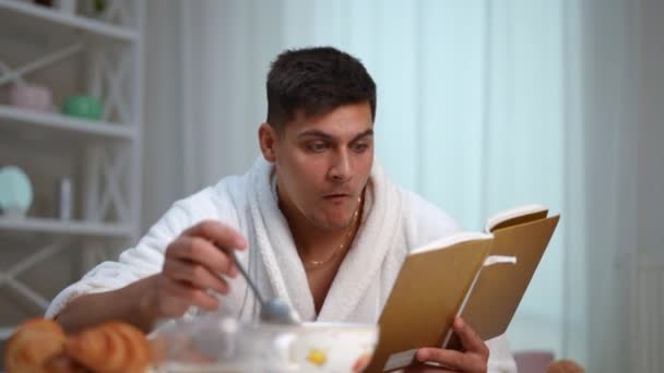 Yemek Yerken Kitap Okumanın Tadını Çıkar Beyaz Bornozlu Genç Bir — Stok video