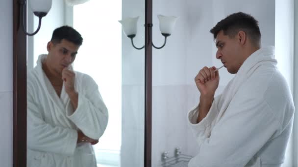 Beyaz Bornozlu Düşünceli Genç Bir Adam Banyoda Bir Duvar Aynasının — Stok video