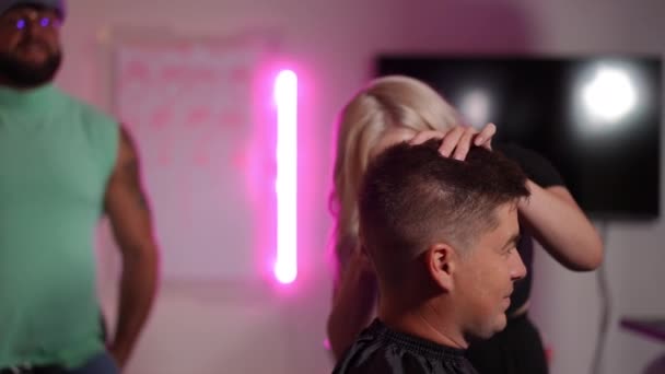 女性の美容師は プロのメンターの緊密な監督の下で男性のクライアントの寺院を剃るためにクリッパーを使用しています 現代美容アカデミーでの美容コース スローモーション — ストック動画