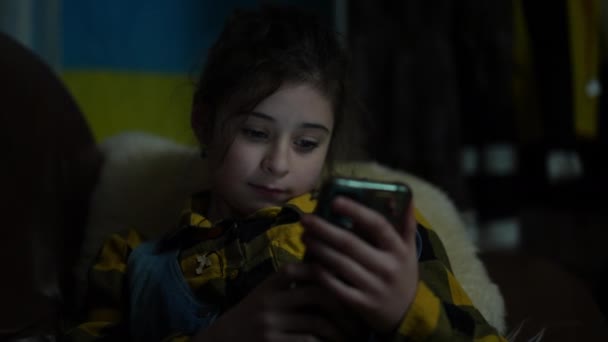 우크라이나의 깃발의 배경에 속에서 소녀는 거실에서 소파에 전화의 화면에 뉴스를보고 — 비디오
