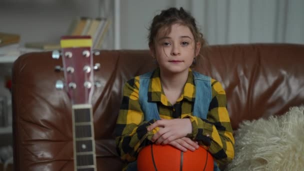Симпатичная Девушка Смотрит Камеру Сидя Кожаном Диване Баскетбольным Мячом Коленях — стоковое видео