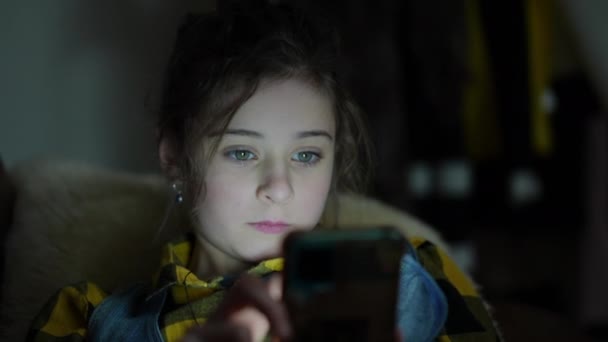 クローズアップ 女の子はモダンな家のリビングルームのソファーの暗闇に横たわって 携帯電話の画面上のインターネットコンテンツを見ます — ストック動画
