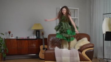 Şık yeşil elbiseli, uzun saçlı güzel bir kız modern bir evin oturma odasındaki deri koltukta gülüyor ve zıplıyor.