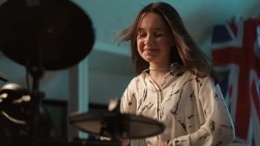 Ağır çekim. Yakın plan. Genç bir müzisyen kız bir müzik okulunun stüdyosunda oturmuş elektronik davul çalarken gülümsüyor ve gülüyor.