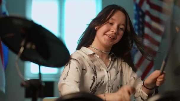 慢动作一个牙齿上戴着牙套的小女孩 一边坐在美国国旗的后面 一边高兴地 精力充沛地在电子鼓机上敲着她的鸡腿 — 图库视频影像