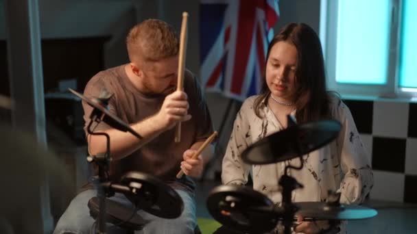 スローモーション 男性の先生は 音楽学校のスタジオに座っている間 彼女がドラムスティックで電子ドラムキットを打つためにどれほど難しいかを弟子に説明します — ストック動画