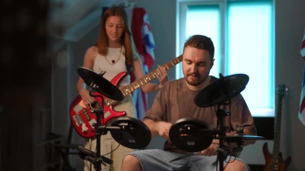 慢动作一个男人坐着弹奏电子鼓 一个年轻姑娘在他身后弹奏低音吉他 音乐学校排练时的节拍 — 图库视频影像