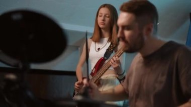 Bir müzik okulunda ritim bölümünün koordineli performansı. Ön planda, biraz odak dışı bir adam dikkatle elektronik davul çalıyor ve genç bir kız bas gitar çalıyor.