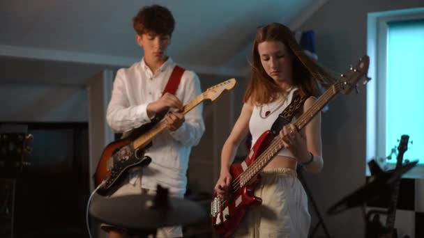 ある男と女の子が音楽学校のレコーディングスタジオで電気ギターを弾いている 若い男が手にピックアップし エレクトリックギターを演奏し 女の子がベースギターを演奏する — ストック動画