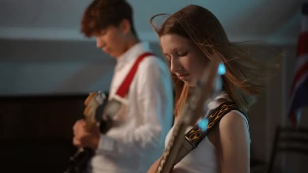 音楽学校でのリハーサルでのギターデュエットのパフォーマンス 前景では 若い赤毛の少女がベースギターを演奏し 男はわずかに焦点を当てて エレクトリックギターを演奏します — ストック動画