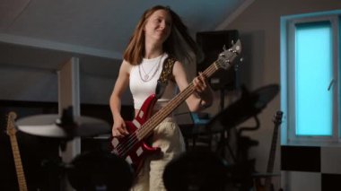 Ağır çekim. Kız bas gitar çalıyor ve müzikten hoşlanıyor. Bas gitarist kız gülerek bir müzik okulunda hit bir beste yapıyor.