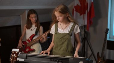 Ağır çekim. Kızlar bir müzik okulunda elektronik müzik enstrümanları üzerinde prova yaparlar. Genç kızlar bas gitar ve sentezleyici çalarlar.