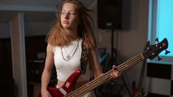 慢动作一个年轻女孩用低音吉他弹奏她最喜欢的摇滚歌曲并面带微笑的肖像 — 图库视频影像