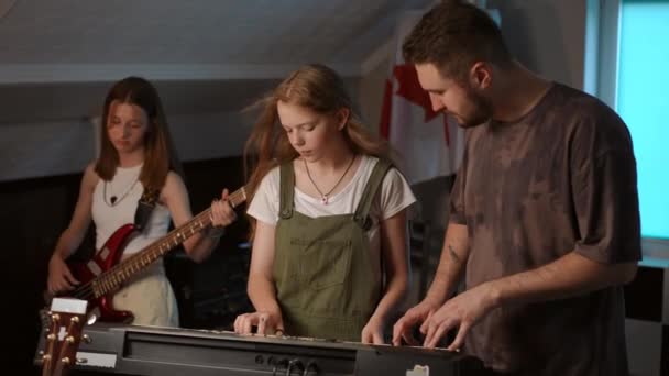 慢动作两名女音乐学校学生和她们的男教师玩电子乐器 一个女孩笑着和老师一起玩合成器 另一个女孩玩合成器 — 图库视频影像