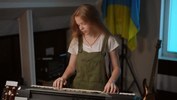 スローモーション 長髪の女の子は 壁にウクライナの旗の背景に対して音楽学校に立っている間 シンセサイザーを演じます 女の子はカメラを見て笑顔で — ストック動画