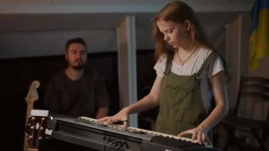 Uzun saçlı tatlı bir kız müzik okulunda donanımlı bir odada duran profesyonel bir müzisyenin gözetiminde bir sentezleyicide bir melodiyi prova ediyor.