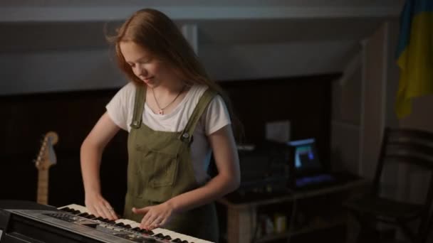 一个长头发的女孩站在音乐学校的教室里 用手捂住合成器上的钥匙 — 图库视频影像
