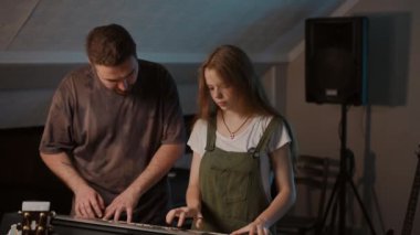 Ağır çekim. Modern bir müzik okulunda modern müzik öğretmenliği. Erkek bir öğretmen müzik okulunda sentezleyici çalan kadın bir klavyeciyi cesaretlendirir ve över.