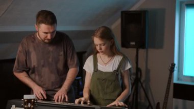 Ağır çekim. Uzun saçlı bir klavyeci kız ve bir erkek öğretmen müzik okulunda dikilirken dört elle sentezleyici çalıyorlar. Modern bir müzik okulunda modern müzik öğretmenliği.
