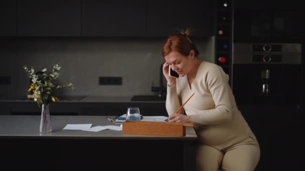 여성은 부엌의 테이블에 앉아서 전화로 이야기하고 수채화가있는 종이에 페인트 브러시로 — 비디오